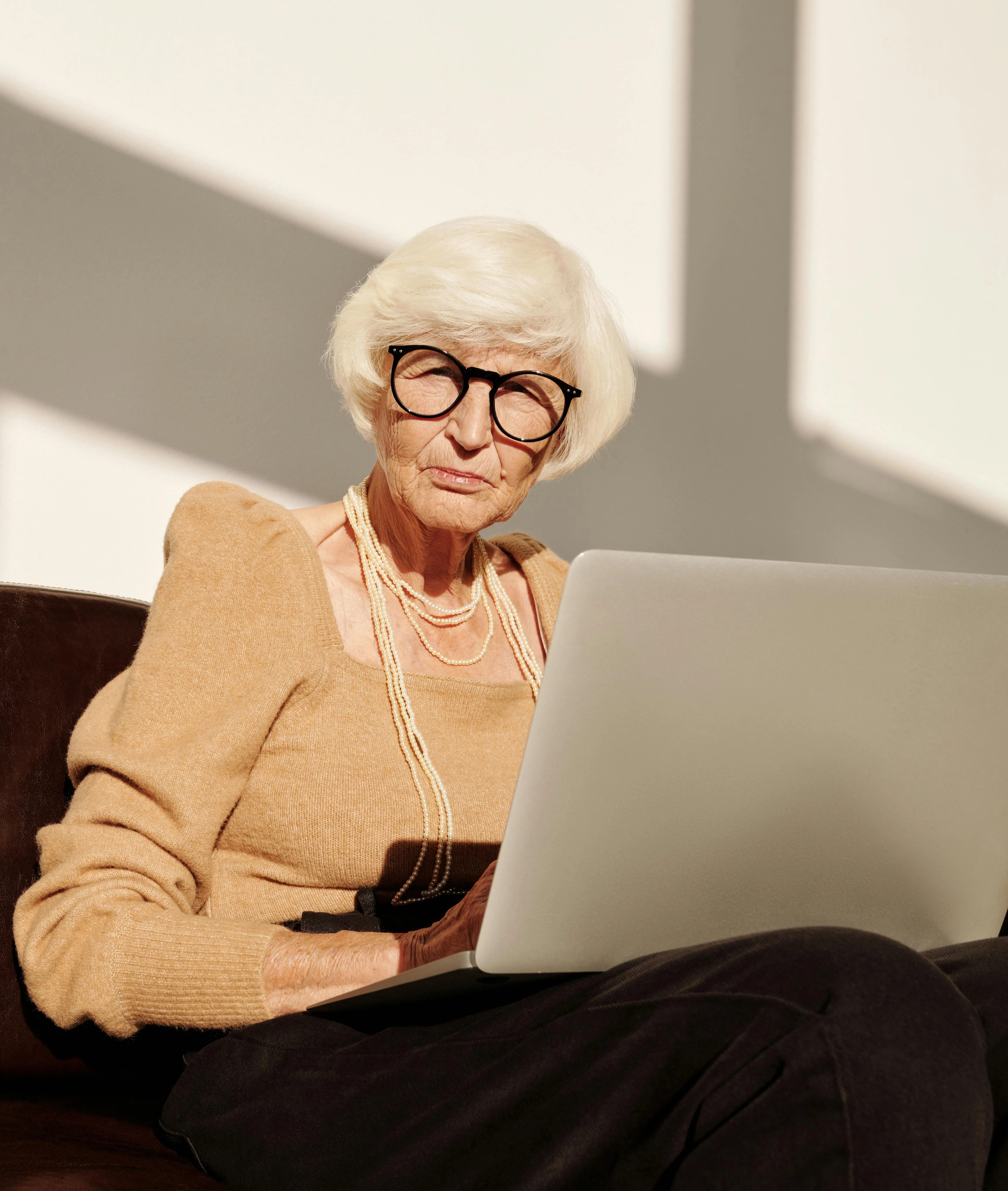 Пожилая женщина с ноутбуком сидит на диване
